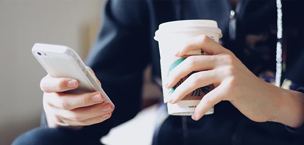 A person holding his smartphone and a cup of coffee